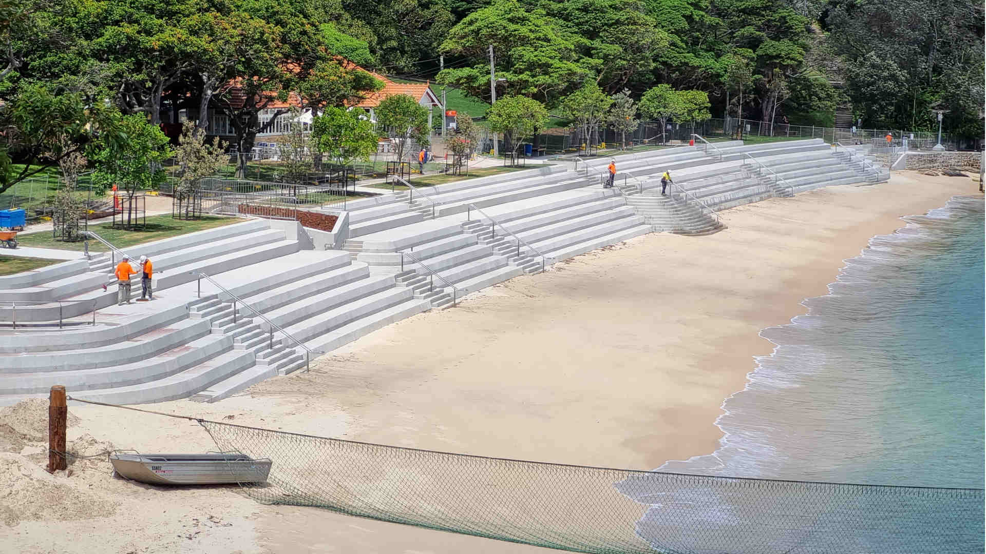 Freshly laid concrete bleachers and promenade along a narrow picturesque beach with a thick treeline in the background