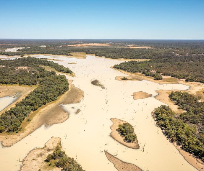 Aerial photograph of a still, sand-coloured river on a long, endlessly flat plain of sand-coloured earth and dark vegetation