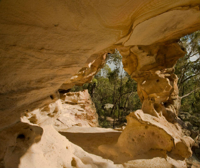 View of the sandstone caves in Warrumbungle National Park. The photo captures the intricate textures and layers of the sandstone formations, with sunlight casting dramatic shadows that highlight the natural beauty and geological features of the caves.