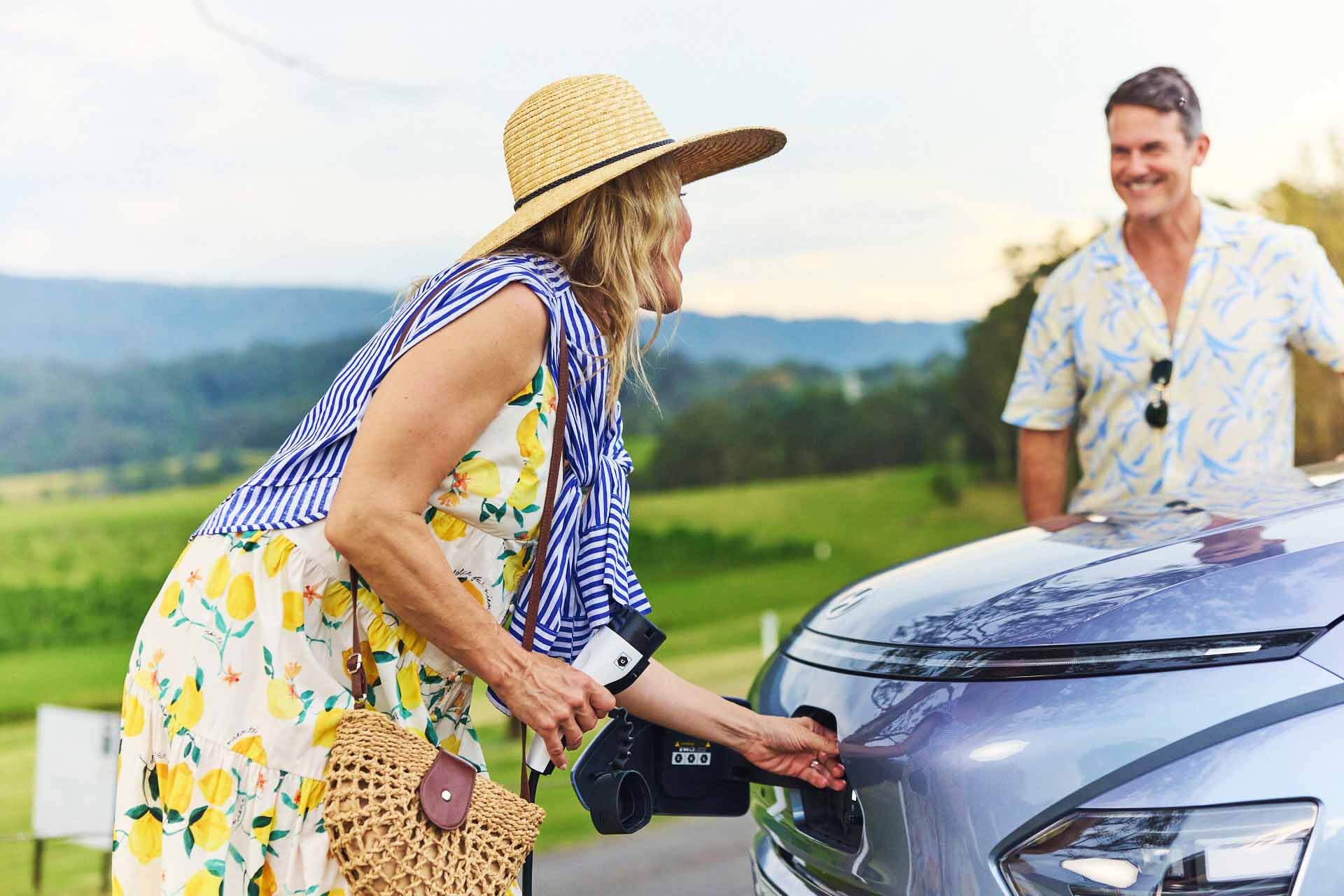 Woman in floral dress cgarges car as man looks on