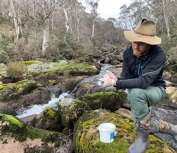 Man with bucket kneeling beside small creek