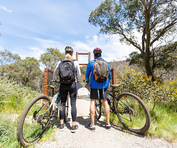 Two cyclists standing with their bikes looking down a path