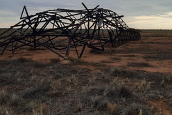 A metal transmission tower lies crumpled on the ground