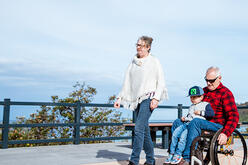 Woman walking next to a man in a wheelchair with a child on his lap.