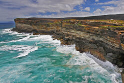 Coastal cliffs at Curracarong with turbulent turquoise sea below and a cloudy blue sky above, showcasing the natural beauty and rugged terrain of Royal National Park.