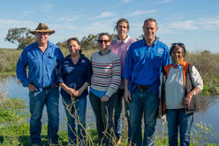 A group of 6 people standing on a natural bank of a creek