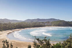 Looking down on the turquoise blue water of Diggers Beach with hills to the north and a clear blue sky above.