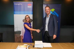 A man and woman shake hands in front of EnergyCo banners, documents on table in foreground