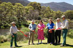 Ministers and NSW National Parks and Wildlife Service staff holding red ribbon pieces beside a tree-lined river