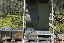 The toilet block is raised a few steps off the ground, and features two silver tanks to the left.